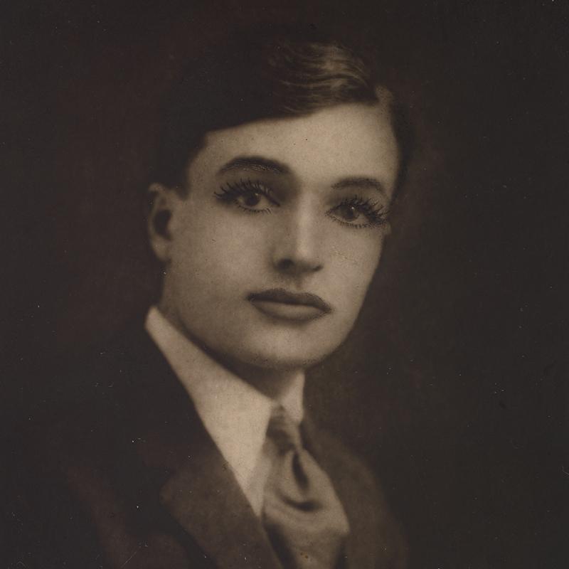 A photograph of a bust length view of a figure wearing dramatized makeup and a masculine suit